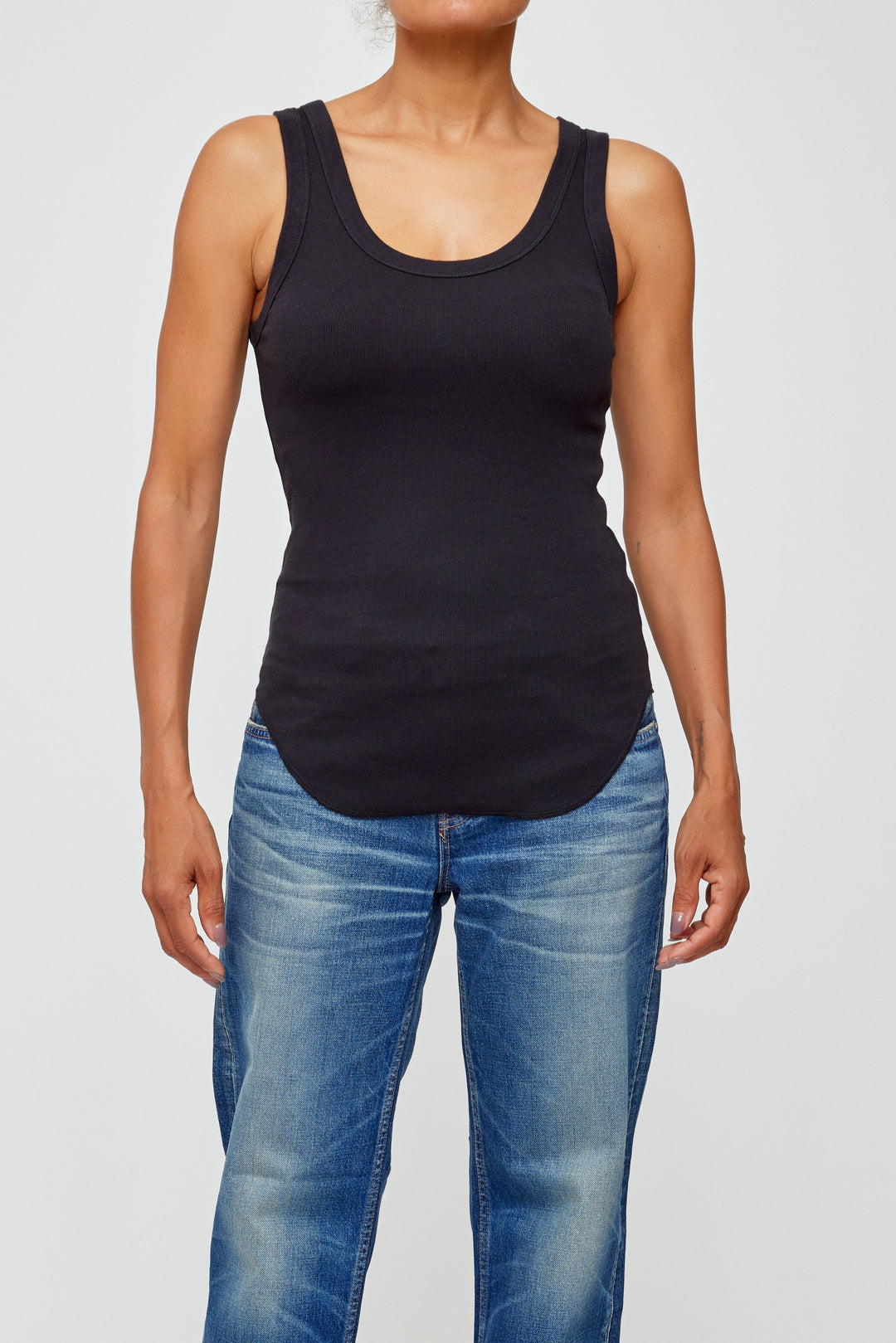 Woman wearing black ribbed tank top with blue jeans on white background