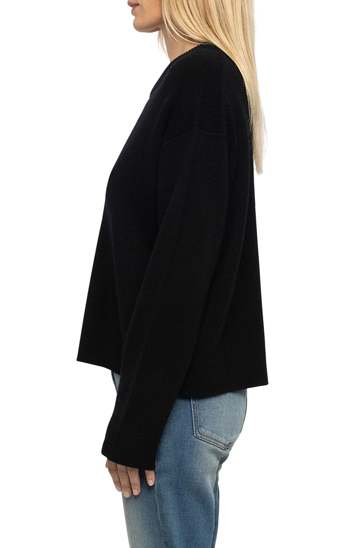 Black oversized knit sweater with long sleeves shown from side angle on model