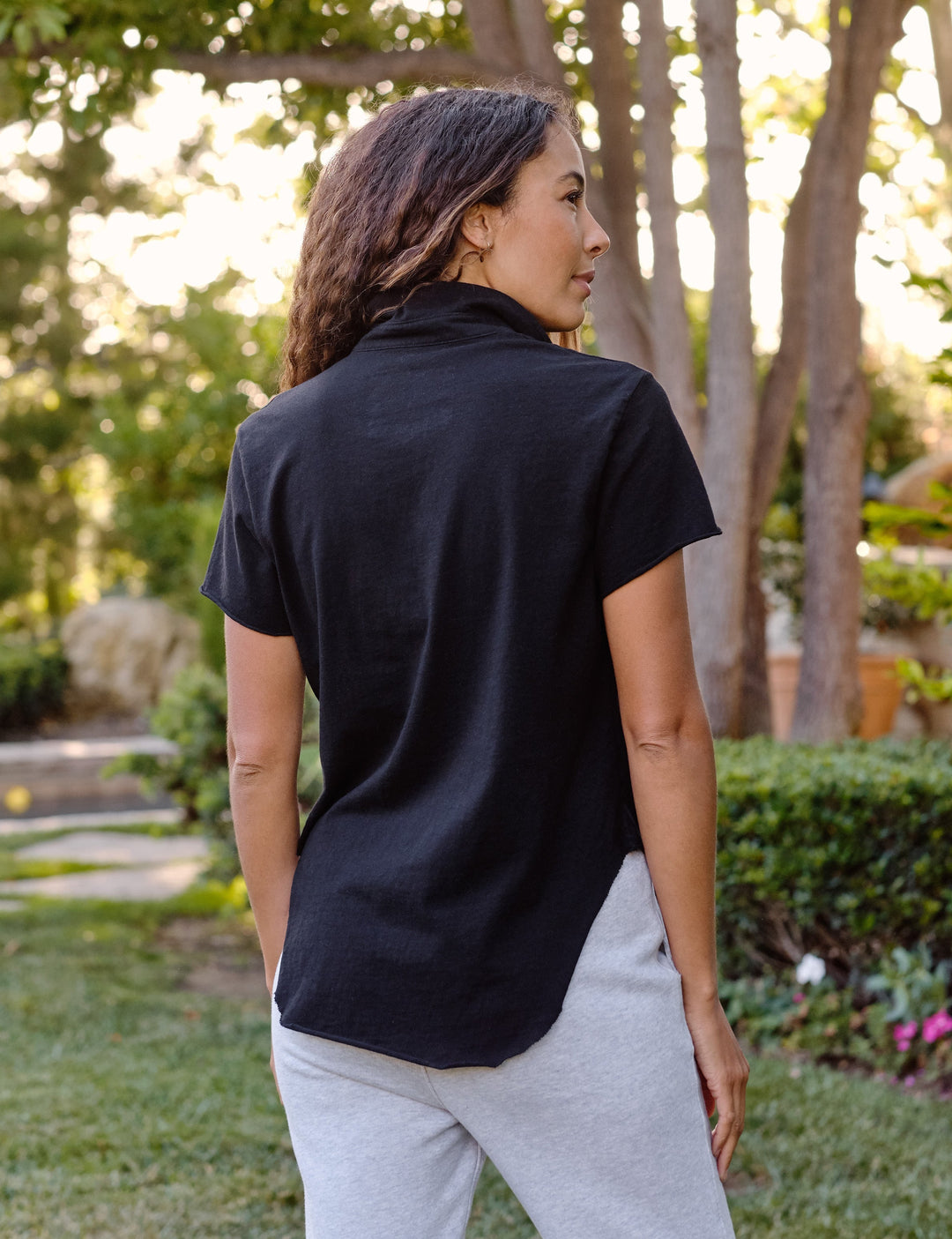 Woman wearing black Frank & Eileen Charlotte Perfect Polo shirt from behind in garden setting