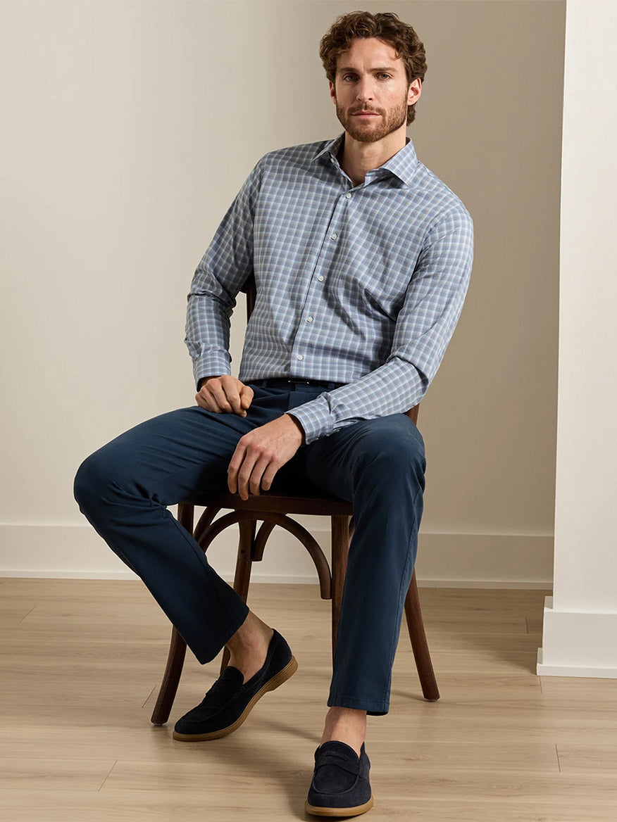 Man seated on wooden stool wearing Peter Millar blue plaid cotton-stretch dress shirt with navy trousers
