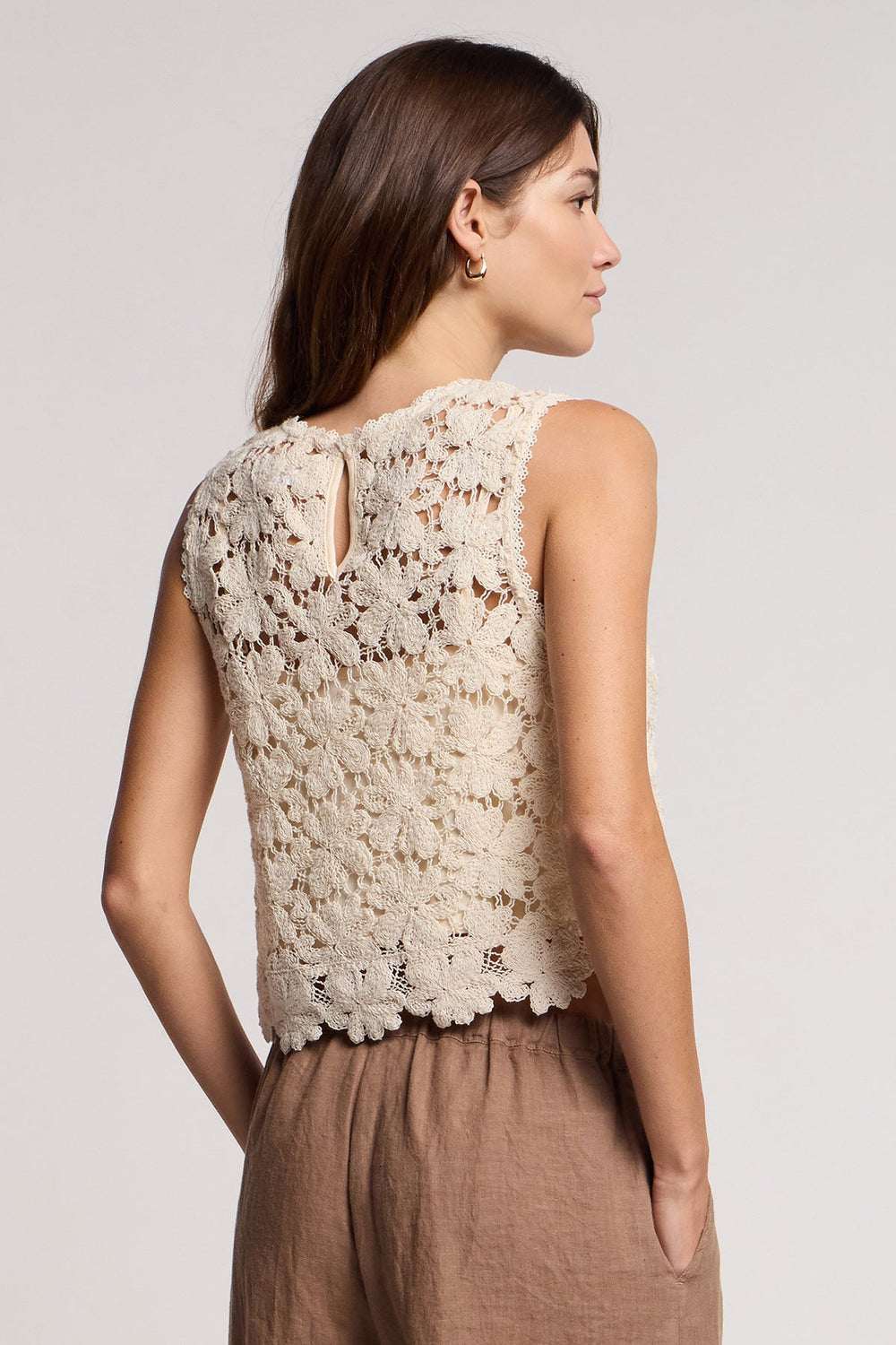 Woman wearing cream lace sleeveless top with brown linen pants, back view